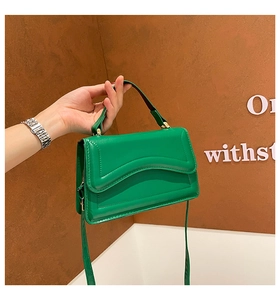 Detail of green handbag with wavy stitching and polished finish in a handheld view