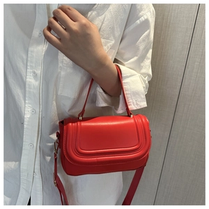 Detail of red leather crossbody square bag featuring a flap closure and adjustable strap