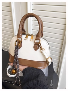 Detail of a beige and brown shell bag featuring dual zippers and woven charm accents