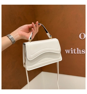 Detailed close-up of a white rectangular crossbody bag with wave-edge flap and gold hardware