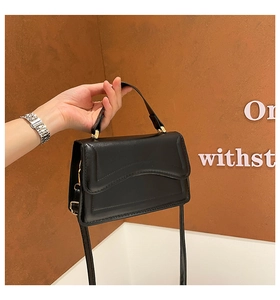 Close-up of black glossy leather handbag with wavy flap and elegant gold metal clasp