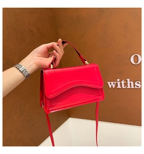 Close-up of a red patent leather handbag with wave flap and gold hardware accents