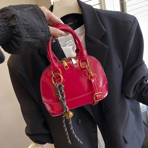 Glossy red shell-shaped handbag with gold hardware and stylish braided bell pendant