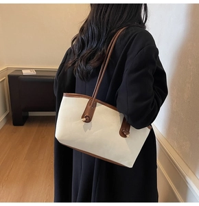 Detail of cream tote bag with brown leather straps shown on model in warm indoor setting