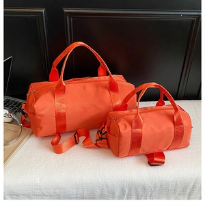 Close-up of vibrant orange cylinder duffel bags in large and small sizes with black straps