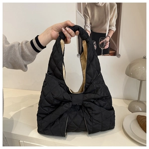 Detail of black quilted puffer tote bag with a large decorative bow and soft nylon texture