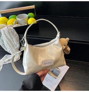 Detail of white glossy cloud bag with cute teddy bear pendant and branded patch