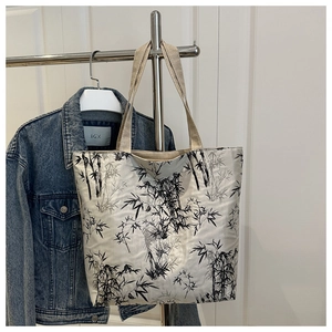 Detailed close-up of ink bamboo pattern on cream tote bag hanging by a denim jacket