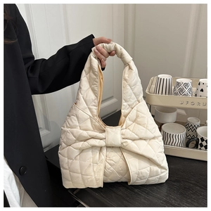 Detail of a beige quilted tote bag featuring a large bow and soft rhombus stitching texture
