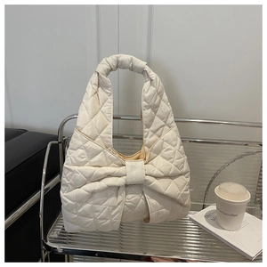 Detail of cream quilted tote bag with large bow design on a stylish shelf