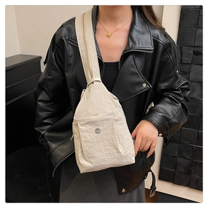 Detail of a beige nylon crossbody bag featuring a front zipper pocket and strap accents