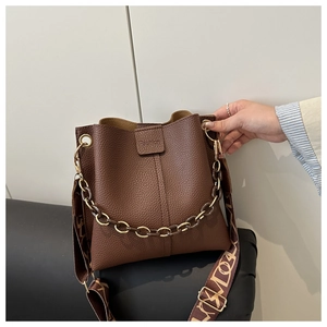 Detailed close-up of dark brown pebble leather texture and golden chain on a bucket bag