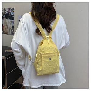 Back view of model wearing a bright yellow lightweight nylon mini backpack with flap pocket