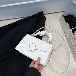 Sac à main blanc matelassé avec boucle dorée et poignée plissée sur fond noir de luxe
