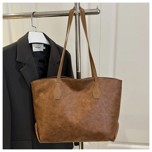Detail view of large brown vintage tote bag with textured finish on a metal stand