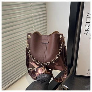Close-up of brown pebble leather bucket bag with gold chain and printed fabric strap