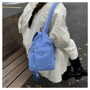 Detailed back view of a light blue nylon backpack with adjustable straps in an outdoor setting