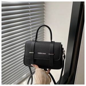 Detail of black box bag showing textured leather flap with metallic bar and fashion text