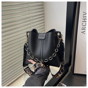Detail of black lychee grain leather bucket bag with chain and geometric fabric strap