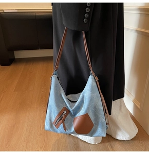 Detail of blue denim tote bag with brown leather straps worn on shoulder by model