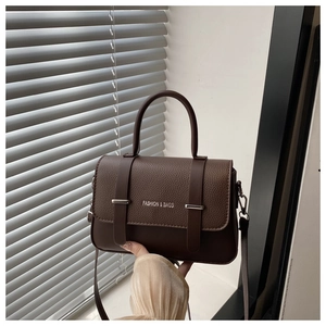 Detail of a brown textured faux leather messenger bag with silver buckles and handle