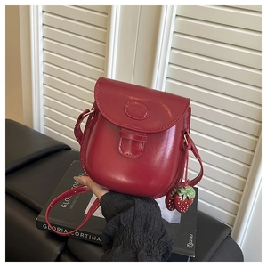 Dettaglio borsa a sella in pelle rossa lucida con ciondolo fragola e tracolla