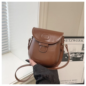 Dettaglio della borsa a tracolla vintage in pelle marrone con patta curva e logo