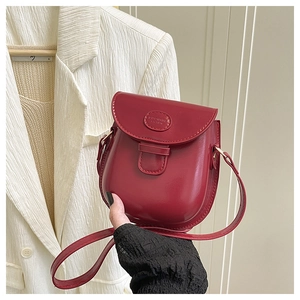 Dettaglio di una borsa a sella in pelle PU rossa lucida con logo ovale in rilievo