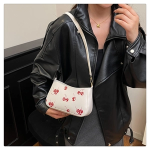 Close-up of white leather underarm bag with red cherry print and gold hardware