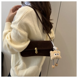 Detail of dark brown velvet baguette bag with gold buckle and plush monster charm