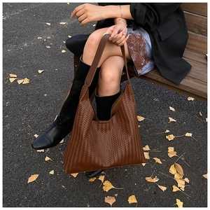 Detailed close-up of brown woven leather tote bag with ginkgo leaf autumn background