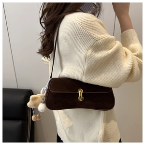 Detail of dark brown suede shoulder bag with gold oval buckle and fluffy charm