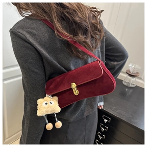Detail of burgundy velvet shoulder bag with gold clasp and cute plush mascot charm