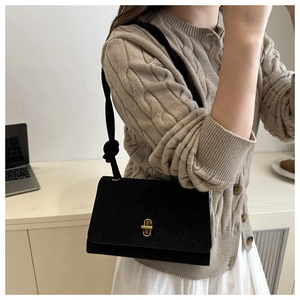 Detail of a black suede messenger bag with gold clasp worn over a beige sweater