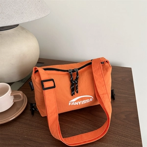 Orange nylon crossbody bag with letter print and adjustable strap on a wood table
