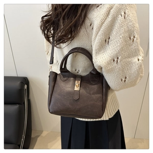 Detail of dark brown leather bucket bag with gold twist lock on knit sweater background