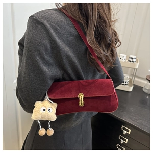Close-up of wine red matte underarm bag with gold lock and plush monster charm