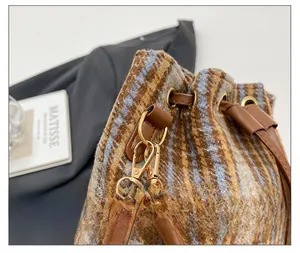 Dettaglio dell'hardware dorato e coulisse sulla borsa a secchiello in lana a quadri e pelle