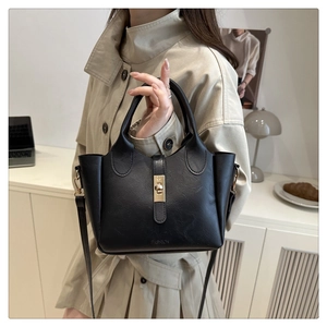Detail of a black leather bucket bag featuring a gold clasp and versatile shoulder strap
