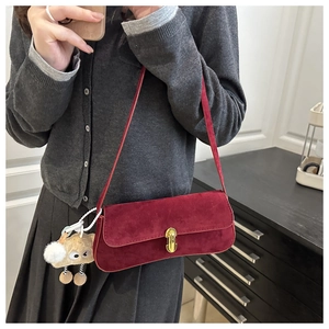 Detail of burgundy suede baguette bag featuring a gold buckle and cute plush charm