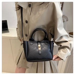 Detail of black leather bucket bag with metal rotary lock and embossed fashion logo