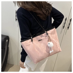 Pink pleated tote bag with black trim and fluffy monster charm shown worn on shoulder