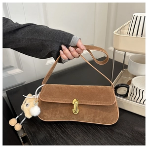 Detailed view of a brown suede baguette bag with gold buckle and plush bear charm