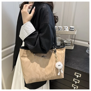 Detailed close-up of large beige tote bag with unique paper-like texture and plush charm