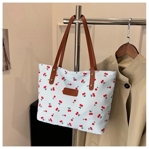Détail du sac cabas imprimé cerise avec poignées en similicuir brun et rivets en métal