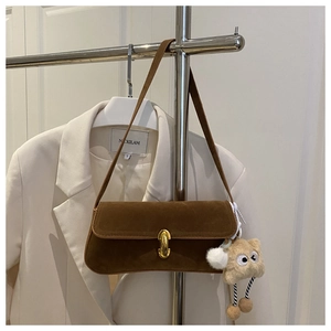 Brown suede baguette bag with a gold buckle and a cute beige plush monster charm detail