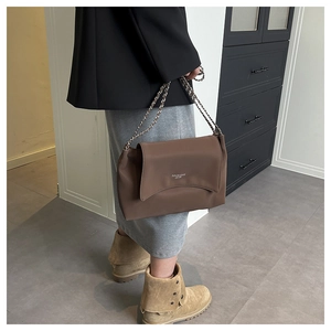 Détail du sac bandoulière en cuir marron avec bandoulière chaîne et logo tendance