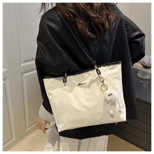Detail of white tote bag with textured surface, black straps and cute plush pendant