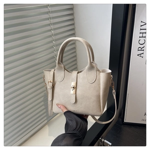 Detail of beige textured bucket bag with gold clasp and embossed fashion logo lettering