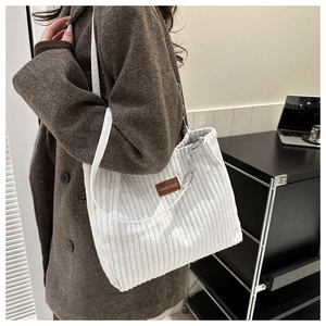 White corduroy tote bag with silver chain detail and leather logo tag on woman coat